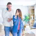 Young,Beautiful,Couple,Standing,At,New,Home,Around,Cardboard,Boxes